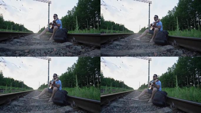 戴着帽子和太阳镜的男人坐在铁轨上弹吉他唱歌