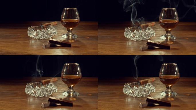 雪茄在一杯威士忌和巧克力棒附近的烟灰缸上慢慢燃烧