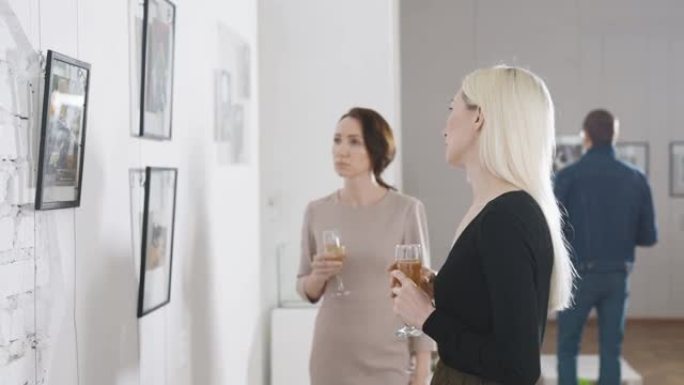 两个朋友在一个美术馆里，在一个当代艺术展览上。女人喝香槟讨论绘画