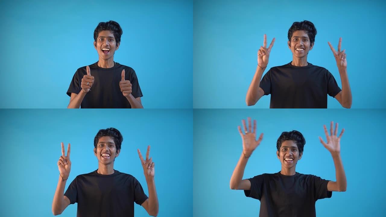 一个穿着黑色t恤的印度男孩在蓝色背景下带着灿烂的笑容享受胜利
