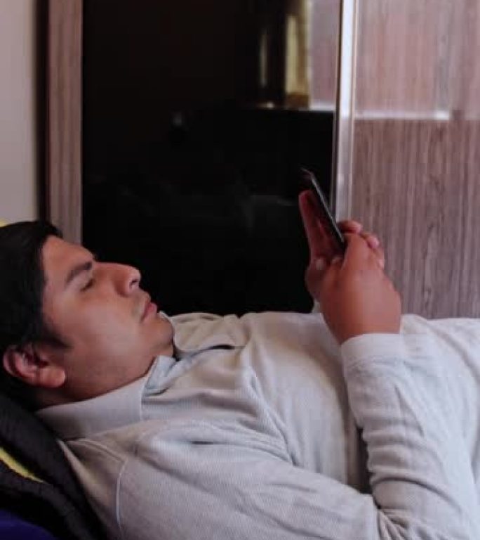 一个西班牙裔男子躺在床上用手机拍摄的垂直镜头，