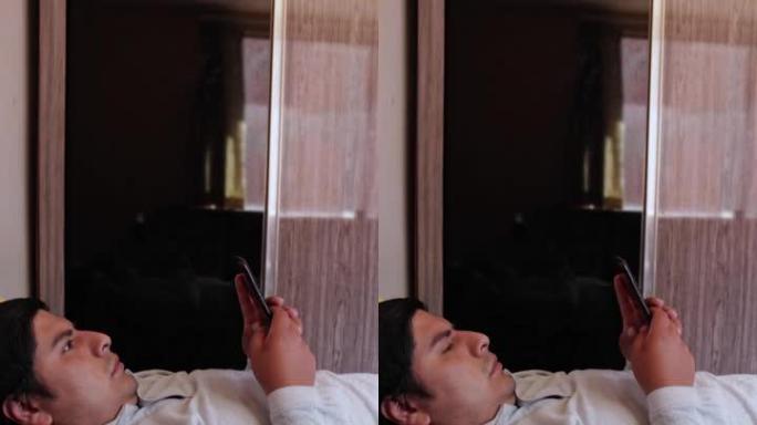 一个西班牙裔男子躺在床上用手机拍摄的垂直镜头，