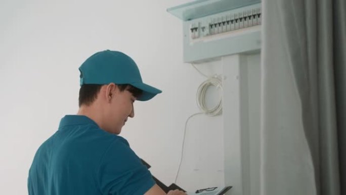 一位穿着蓝色制服的亚洲年轻技术人员正在检查电器