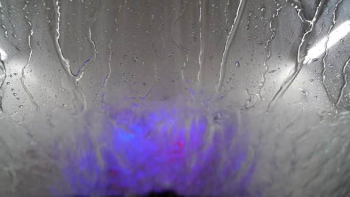 当汽车在洗车场冲洗并驶入干燥区域时，您可以透过汽车的挡风玻璃看。水滴在挡风玻璃上移动。