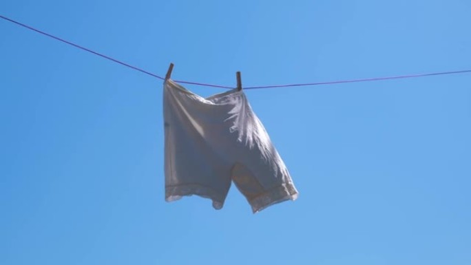 老式白色短裤在绳索上对着天空干燥，随风摇曳。慢动作。