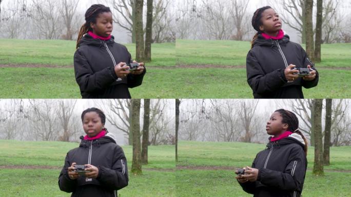 年轻的非洲女孩站在寒冷的天气里检查在公园户外飞行的4k无人机。