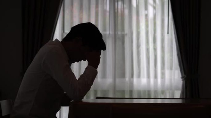 一个悲伤的男人坐在黑暗中的剪影，家庭暴力，家庭问题，压力，暴力，抑郁和自杀的概念