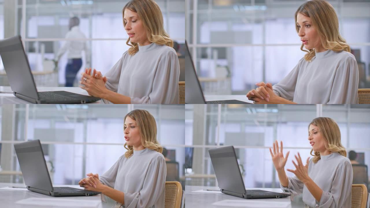 一名年轻女子坐在办公室里，在笔记本电脑上通过可视电话开会