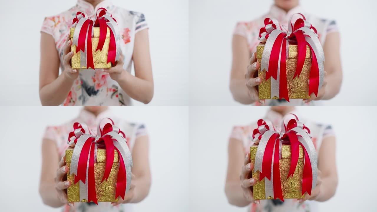 中国/亚洲妇女在春节期间，穿着旗袍白色连衣裙，用一盒金色的大礼物送给家人，亲戚和朋友，以庆祝新年快乐