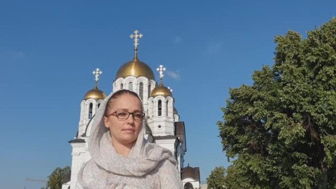 俄罗斯东正教徒戴围巾的中年妇女站在东正教会的背景上