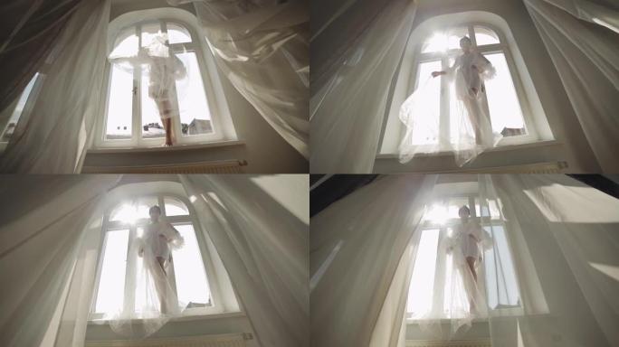 穿着闺房礼服的新娘留在窗台上婚礼晨间准备穿着睡衣，面纱的女人