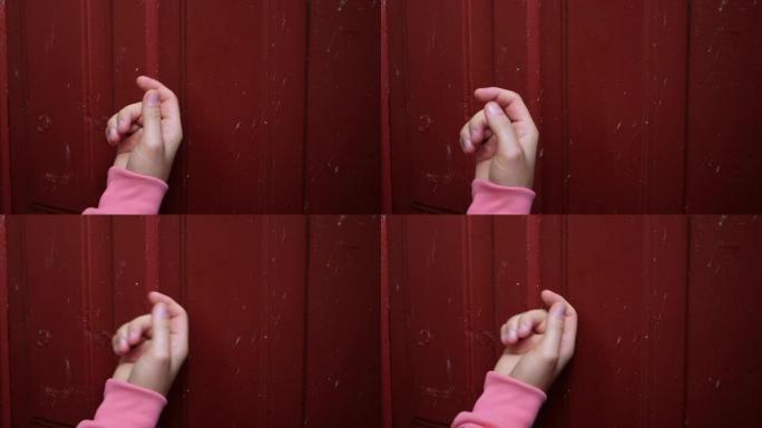 一个粉红色袖子的年轻人的手在慢动作中敲开了一扇木制的红色门