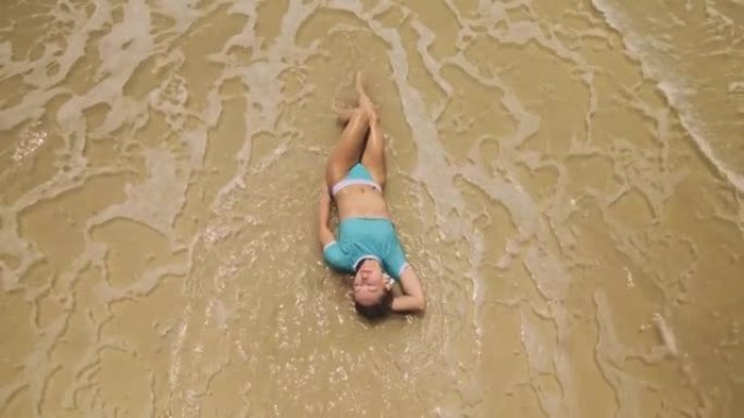 女人躺在浅水大海上。一个醉醺醺的女人正在热带岛屿上享受她的假期。女孩有趣摆姿势。俯视图