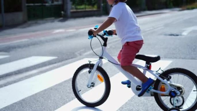 带自行车和头盔的儿童过街。在城市街道人行横道上骑带轮子的运动儿童自行车