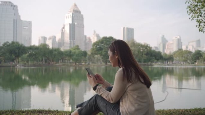 亚洲妇女很高兴通过早上在城市公园的电话在线聊天来放松身心，人们在城市自然环境中放松身心