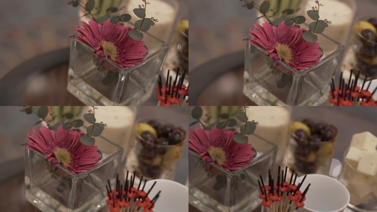 桌子上摆着鲜花和一些带有开胃菜的小吃的玻璃花瓶的特写镜头