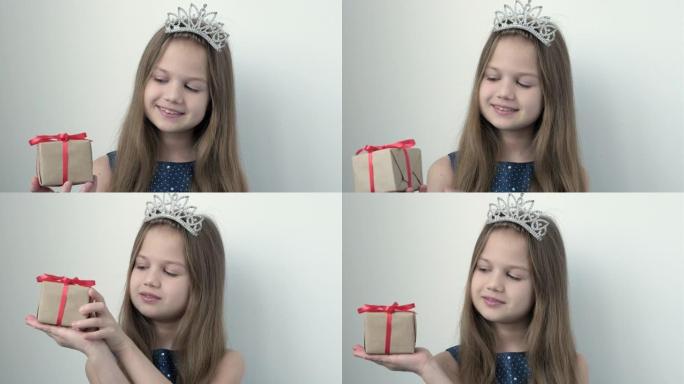 穿着公主皇冠和蓝色节日礼服的微笑小女孩展示礼物