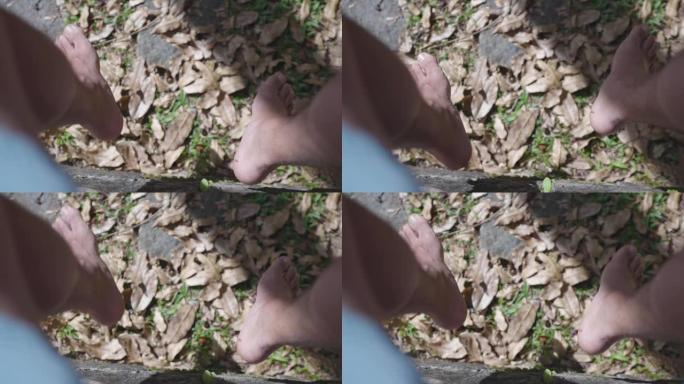 一个人的高角度视图，他的脚在覆盖着干燥的落叶的地面上摆动