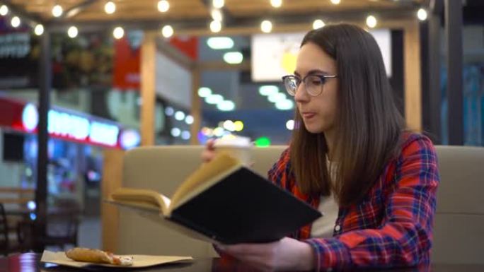 一个年轻女子正在舒适的咖啡馆看书。一个女人坐在餐桌旁，在美食广场吃披萨。穿着红色衬衫戴着眼镜的女孩。