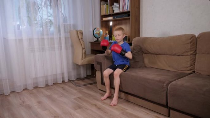 一个小男孩在家里的沙发上戴上拳击手套。