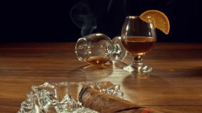 烟灰缸，配有点燃的雪茄，被推翻的玻璃杯以及一杯威士忌和橙子