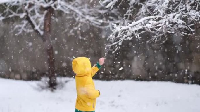 穿着黄色冬装的有趣小男孩在降雪时行走。孩子们的户外冬季活动。