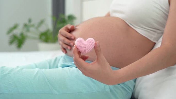 怀孕爱婴概念。孕妇将心脏延伸成粉红色，并向未出生的孩子表示爱。粉红色的心代表了女人对孩子重要性的感受