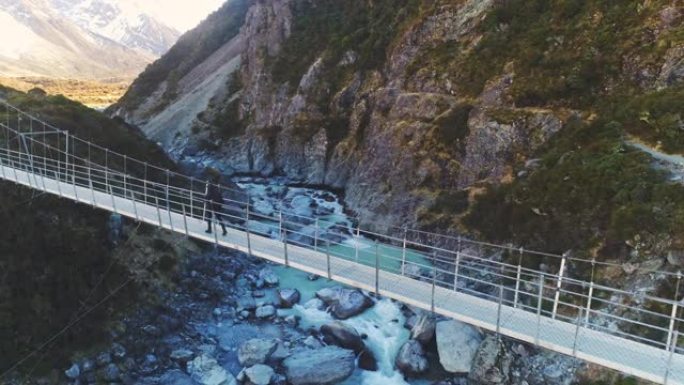 徒步旅行者沿着悬索桥漫步，冲向急流的河水，到达雪山