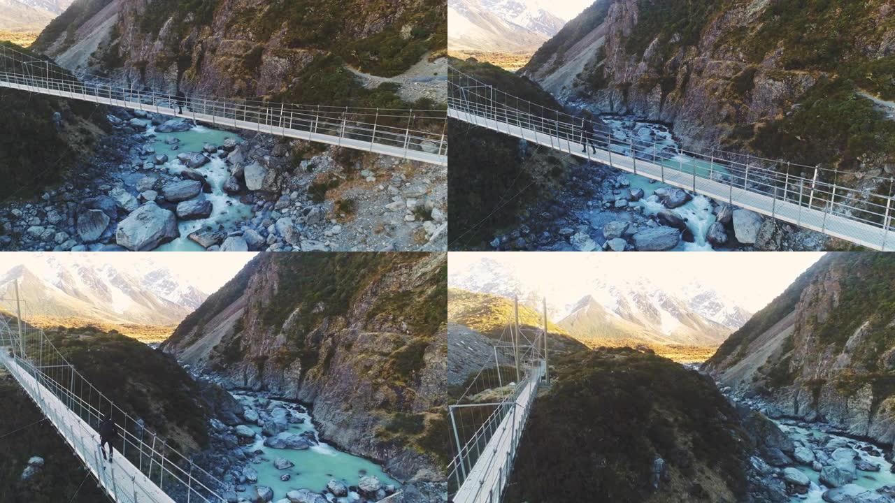 徒步旅行者沿着悬索桥漫步，冲向急流的河水，到达雪山