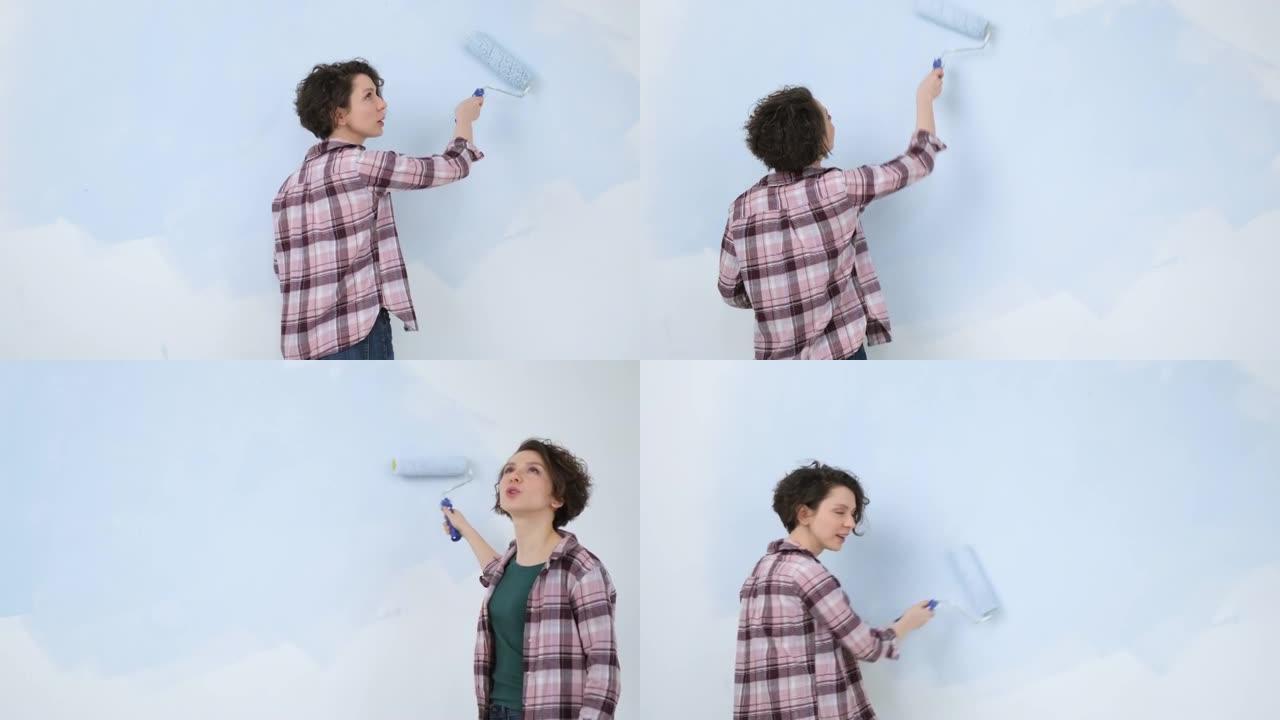 一个年轻的成年快乐的女人，用滚筒涂蓝色油漆。家庭房间公寓设计的维修和翻新。DIY修理房子。
