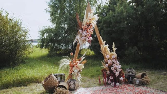 户外婚礼上的特写美丽波西米亚拱门装饰。柔和色彩的花卉组合物，干花，木椅和老式地毯。夏季婚礼。