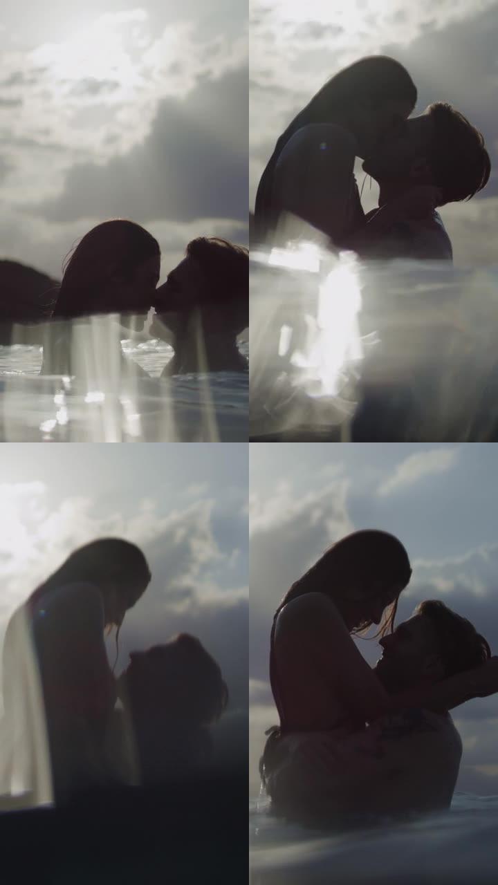 浪漫的异性恋夫妇在日落时一起在海里游泳。在水中接吻和玩耍垂直视频