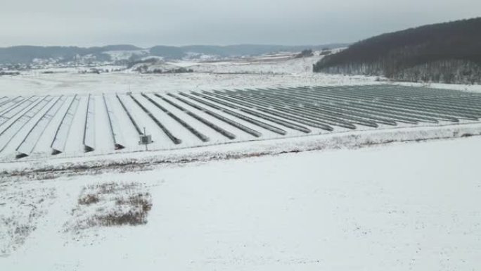 白雪覆盖的可持续发电厂的鸟瞰图，带有许多排的太阳能光伏板，用于产生清洁的电能。冬季可再生电力的低效性
