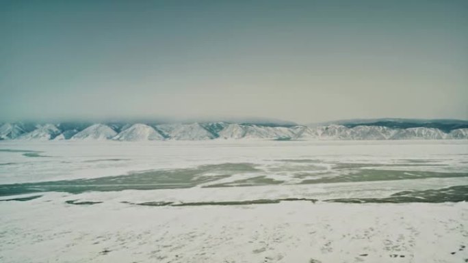 在贝加尔湖上空缓慢飞行。湖被雪覆盖，在一些地方你可以看到裸露的冰，在背景是山脉。奥尔洪岛，小海的海峡