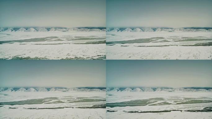 在贝加尔湖上空缓慢飞行。湖被雪覆盖，在一些地方你可以看到裸露的冰，在背景是山脉。奥尔洪岛，小海的海峡