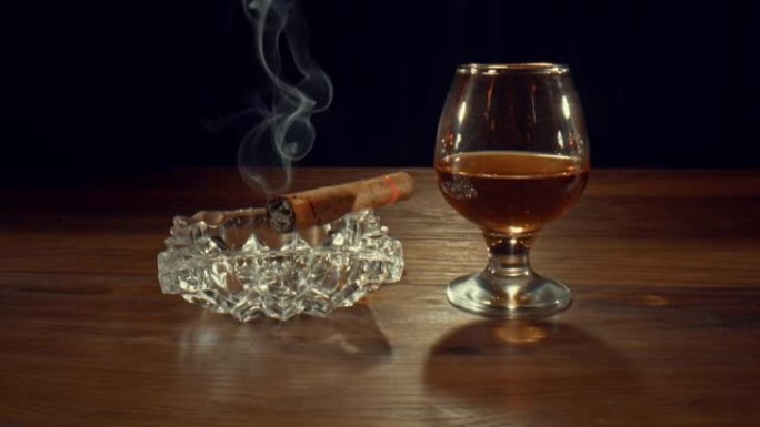 雪茄在一杯威士忌附近的烟灰缸上慢慢燃烧