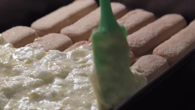 准备提拉米苏蛋糕，在预先制作的饼干上涂上奶油。特写。