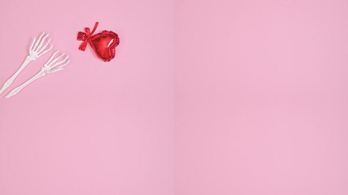 气球心从柔和的粉红色背景上的骷髅手中飞过。停止运动。平铺