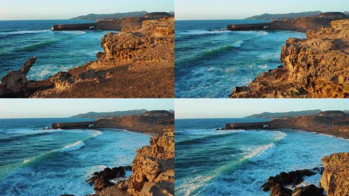 飞越巨大的海浪在巨大的岩层中撞击。日落之光。绿松石水发泡。空中。带洞的砂岩悬崖，陡峭的海滩。户外旅行