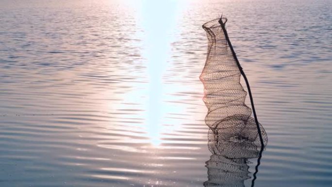 渔网笼位于河流或池塘的岸边。钓鱼陷阱里有一些鱼。钓鱼笼在平静的湖面上。鱼的渔网位于海岸附近的浅水上