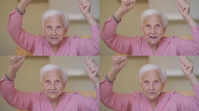 白发苍苍的快乐老妇人的肖像，灰色的眼睛看着相机，在电视上观看比赛。开朗积极的高加索退休人员在室内摆姿