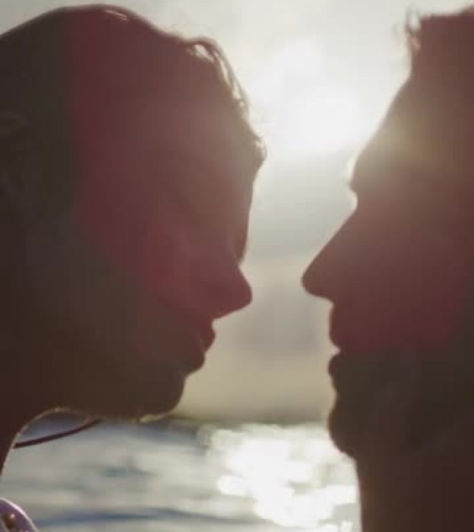 浪漫的异性恋夫妇在日落时一起在海里游泳。在水中拥抱和亲吻垂直视频