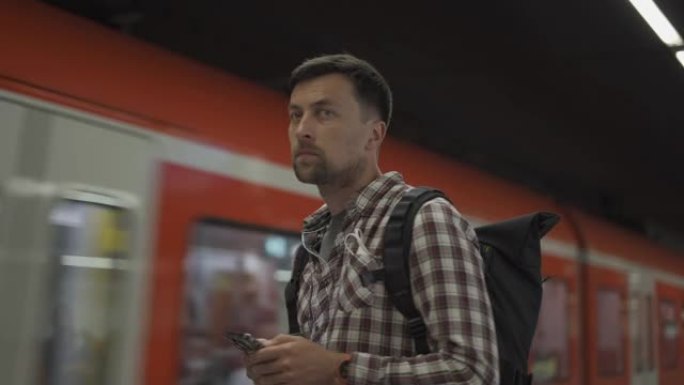 德国慕尼黑，一名男子在路过的火车前带着智能手机。带背包的乘客使用电话创建路线图并在线购买机票。S-B