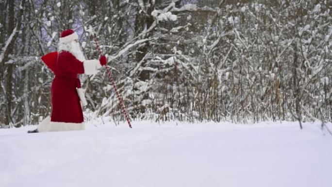 圣诞老人带着魔法杖和一袋圣诞礼物走在雪林里。