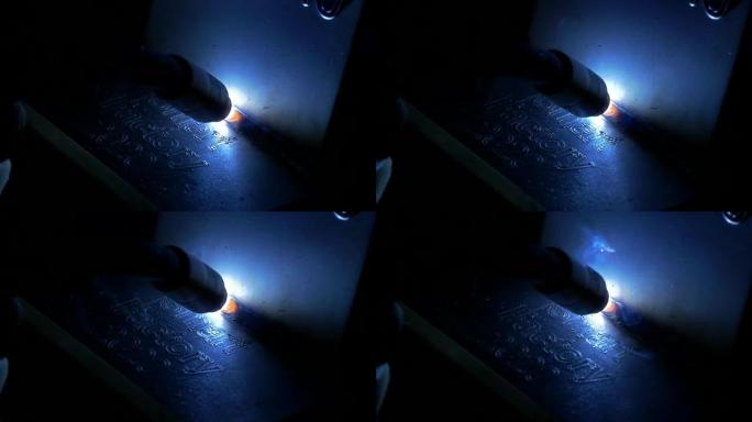 运动中的焊接工具的特写镜头，在黑暗的工厂中反射白光和火花