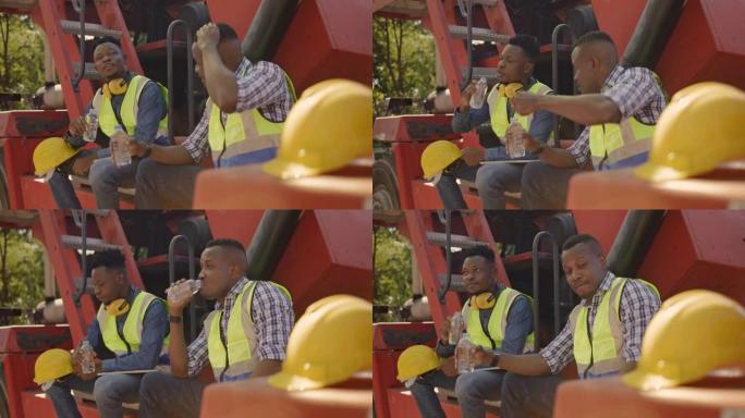 两名非裔美国建筑工人高兴地坐在叉车上喝水，并在工作施工期间与他们交谈。工头与下属友好地提供建议。团队