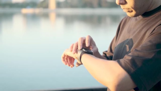 亚洲男性在早晨日出时在公园跑步进行锻炼，使用智能手表按start记录并观察心率以保持健康。