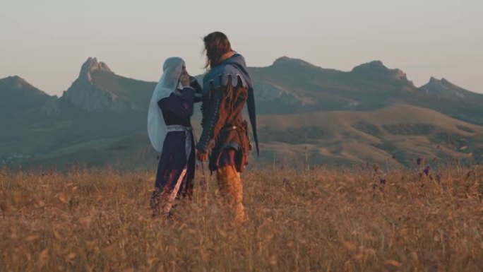 一对恋爱中的夫妇，一个穿着中世纪服装的男人和一个女人，在山里夕阳的映衬下。慢动作侧视图