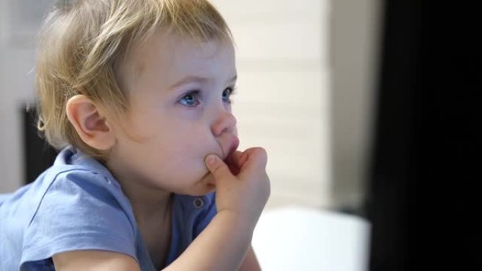 小女孩专心地盯着监视器。一岁的小孩看着笔记本电脑屏幕，做鬼脸。蹒跚学步的孩子坐在桌子旁，看着儿童卡通