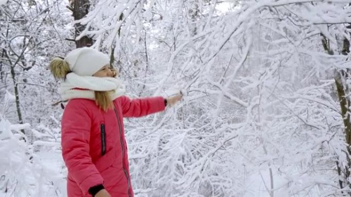 一个年轻积极的女孩在降下的雪中真诚地欢欣鼓舞。她微笑着摇着树上的雪。